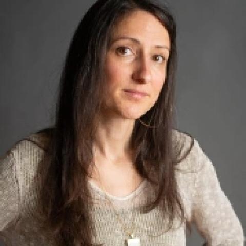 Carolyn has long brown hair. She is light or white skinned and wears a cream sweater in front of a grey backdrop.
