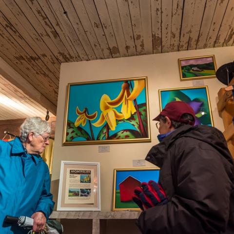 A group of people observe a painting of yellow flowers in a gallery space.