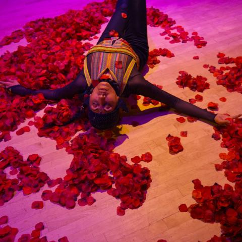 A woman leans over a pile of rose petals on wood floor.