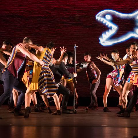 A group of dancers perform below a light up piranha.