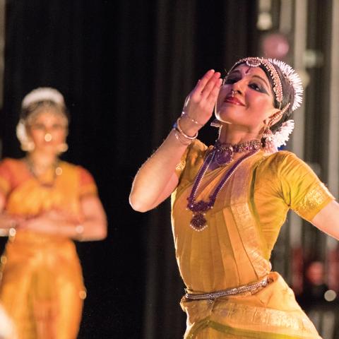 A woman in traditional Indian garb and decoration performs with others similarly adorned.
