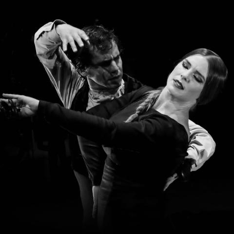 In black and white, a man and a woman dance with hand gestures.