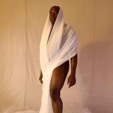 A Black person is wrapped in a white sheer fabric.