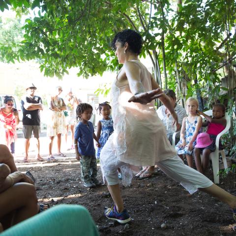 Outside and surrounded by a crowd of kids and adults, a woman leans on her front legs and throws her arms back.