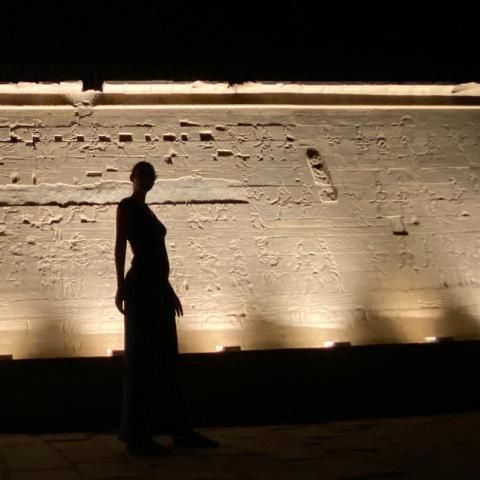Silhouette of a woman, in front of a cream, stone wall that is underlit.