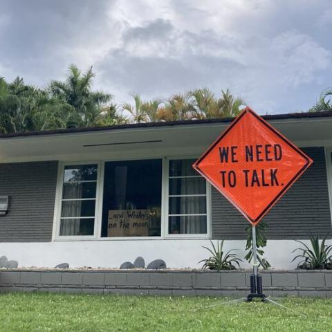In front of a one story home, a traffic sign reads: We Need to Talk.