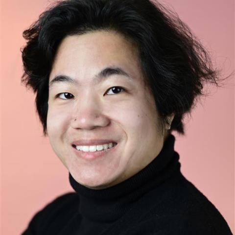 Llewellyn has hair that hits at his cheek bones. He wears a black turtleneck in front of a peach backdrop.