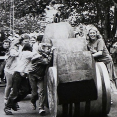 In black and white: women push sculptures on wheels down a street.