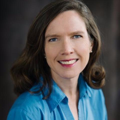 Woman in a blue button down with red lipstick  smiles.