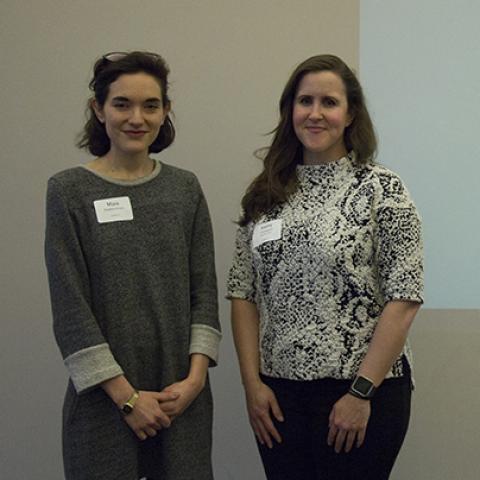 Two women pose in front of a slide from their presentation